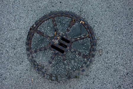 Sewer manhole on the urban asphalt road. Closeup photoの写真素材