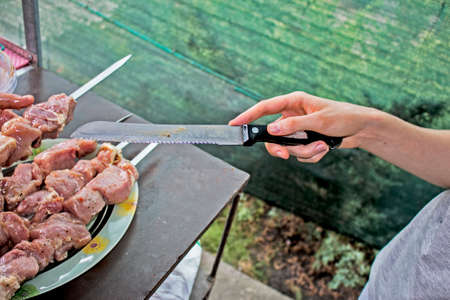 A woman is stringing juicy meat on a skewer. Cooking barbecue in nature