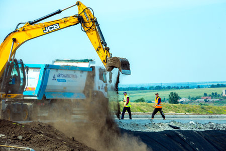 Dnepropetrovsk, Ukraine - 08.17.2021: The excavator works at a construction site in earthworks. Excavator on road works digs the ground. Construction equipment for earthworksのeditorial素材