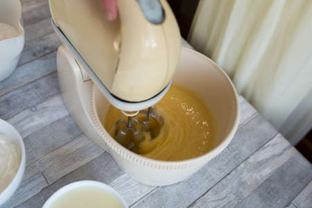 Cake making process. Female hands use a mixer to beat eggs and sugar in a bowl to make dough. Step by step recipe for chocolate cake. Series. Baking concept.の写真素材
