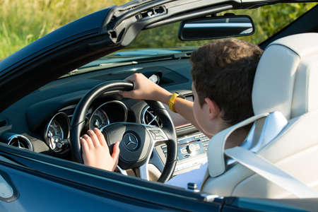 Dnepropetrovsk, Ukraine - 08.24.2021: Closeup on male hands driving Mercedes Benz car luxury transportation lifestyle. Mercedes Benz SL550 convertible on the road.のeditorial素材