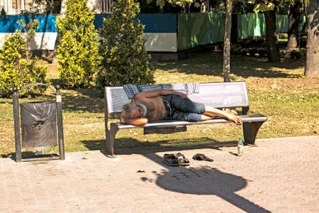 Dnepropetrovsk, UKRAINE - 09.13.2021: A homeless beggar sleeps on a park bench. Social problem. Beggars - unemployed, refugees, emigrants.のeditorial素材