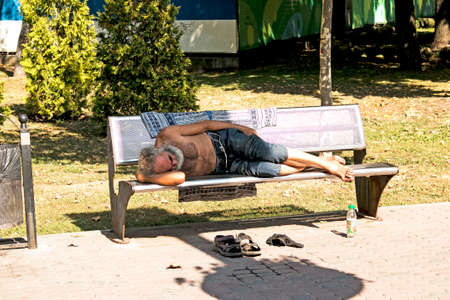 Dnepropetrovsk, UKRAINE - 09.13.2021: A homeless beggar sleeps on a park bench. Social problem. Beggars - unemployed, refugees, emigrants.のeditorial素材