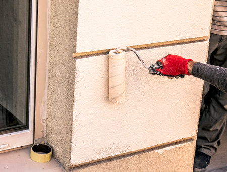 Male hand with a roller paints the wall with beige paint. Preparing the outer wall of the building for winter.の写真素材