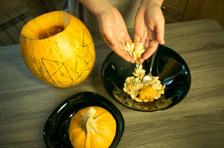 Halloween. Making Jack O'Lantern at home. Pumpkin preparation process. Women's hands take out seeds from a pumpkin.の写真素材