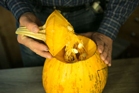 Halloween. How to make Jack O'Lantern at home? Male hands with knife, leftovers of pumpkin on the kitchen table. Selective focus and bokeh.の写真素材