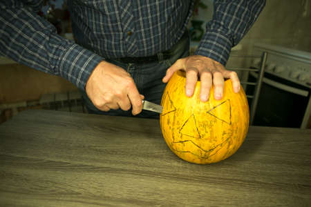 Halloween. How to make Jack O'Lantern at home? Male hands with knife, leftovers of pumpkin on the kitchen table. Selective focus and bokeh.の写真素材