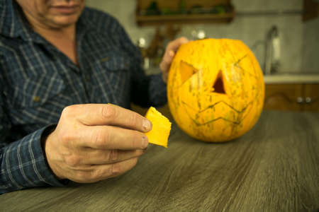 Halloween. How to make Jack O'Lantern at home? Male hands with knife, leftovers of pumpkin on the kitchen table. Selective focus and bokeh.の写真素材