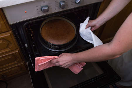 A step-by-step process for making a sour cream chocolate cake. Women's hands get the finished cake out of the oven. Baking concept.の写真素材