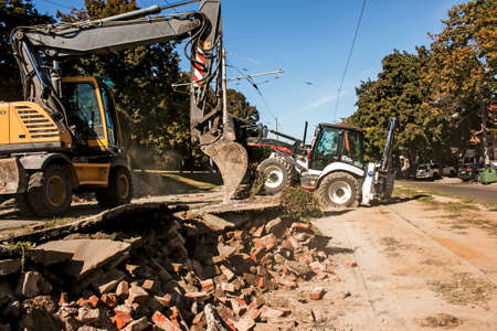 Excavator, grader and workers remove debris after dismantling a tram stop. Works on tram tracks.