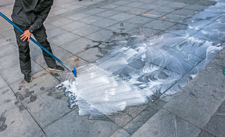 An employee washes the surface of the sidewalk with a mop. The man uses foam with water for cleaning. Urgent cleaning on the street. A large mop in the hands of a worker.の写真素材