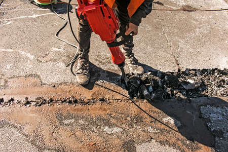 A worker repairs the road surface with a jackhammer on a summer day. Construction works on the road.の写真素材