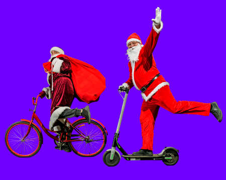 Two merry Santa Clauses in Christmas hats and red suits ride a scooter and a bicycle with bags of...