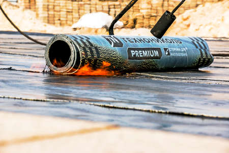 Dnepropetrovsk, Ukraine - 10.28.2021: The process of installing roofing material using a blowtorch. The bituminous felt melts during the installation process. Soft roof.のeditorial素材