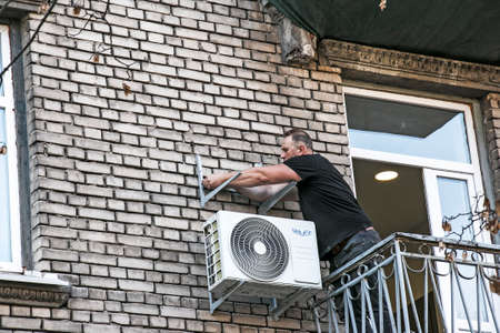 Dnepropetrovsk, Ukraine - 10.22.2021: A worker installs the bracket for the outdoor unit of the air conditioner on the wall of the house.のeditorial素材