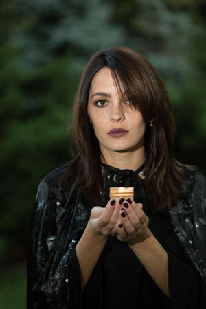 Portrait of an attractive young woman in a black dress with a cape. In the hands of a burning...