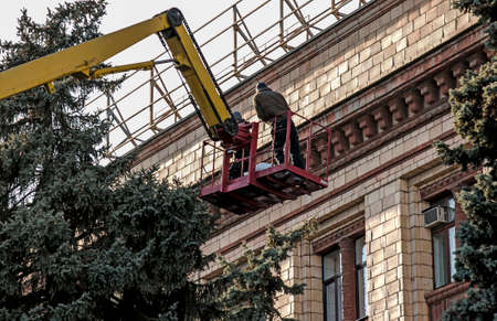 Preparation of city streets for the New Year. Workers at a height in a crane basket prepare trees...