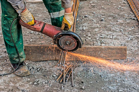 A male hand cuts off pieces of reinforcement using an angle grinder. Cutting steel interspersed with sparks on a construction site. Sparks when cutting metal with an angle grinderの写真素材