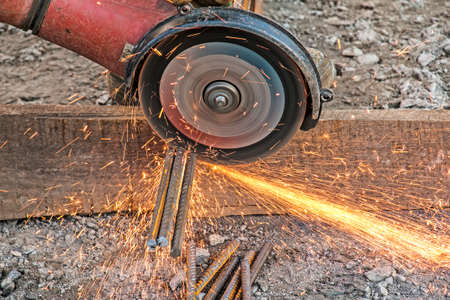 A male hand cuts off pieces of reinforcement using an angle grinder. Cutting steel interspersed with...
