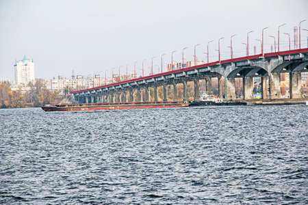 An articulated tug and bulk barge transport sand and construction materials along the river. A large barge sails along the wide Dnieper River. Transport industry. Landscape.のeditorial素材