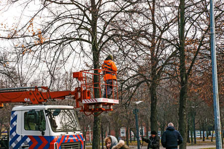 Dnepropetrovsk, Ukraine - 11.22.2021: Municipal workers on a truck crane decorate city streets with Christmas lights. High-altitude work in cloudy weather.のeditorial素材