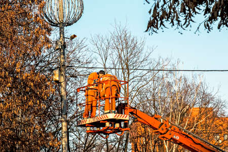 Dnepropetrovsk, Ukraine - 11.24.2021: Municipal workers on a truck crane decorate the city streets with Christmas lights. High-altitude work in sunny weather.のeditorial素材