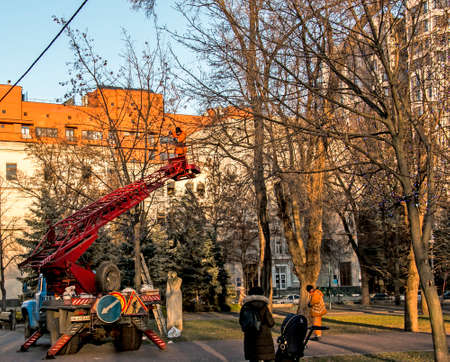 Dnepropetrovsk, Ukraine - 11.24.2021: Municipal workers on a truck crane decorate the city streets with Christmas lights. High-altitude work in sunny weather.のeditorial素材