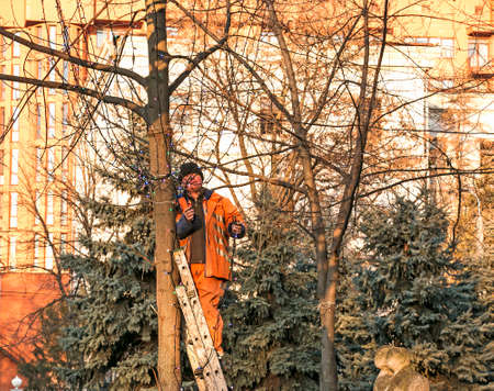 Dnepropetrovsk, Ukraine - 11.24.2021: Municipal workers on a truck crane decorate the city streets with Christmas lights. High-altitude work in sunny weather.のeditorial素材