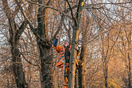 Dnepropetrovsk, Ukraine - 11.24.2021: Municipal workers on a truck crane decorate the city streets with Christmas lights. High-altitude work in sunny weather.のeditorial素材