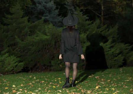 A woman in a black hat and black dress in full growth with her back to the camera. Fashionable girl...