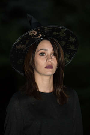 Portrait of a young woman in a pointed wide-brimmed hat. The girl is wearing a black dress. Emotion...