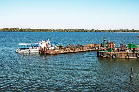 Cleaning the newly formed island from industrial waste on the Dnieper with a dredger. A barge with a...