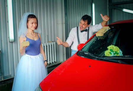 A young man with a bow tie and a woman in a veil are washing a car at a car wash. wedding anniversary. Humor.の写真素材