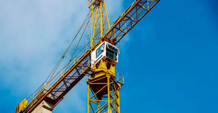High-rise construction crane with a long yellow boom against the blue sky.のeditorial素材