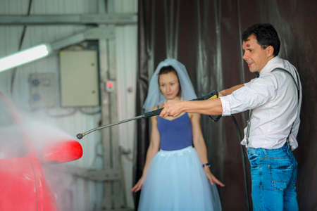 Portrait of a young couple in wedding attire celebrating their wedding anniversary. The couple is washing the car. Smile, kiss, loveの写真素材