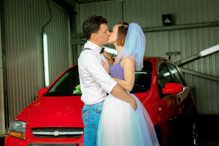 Portrait of a young couple in wedding attire celebrating their wedding anniversary. The couple is washing the car. Smile, kiss, loveの写真素材