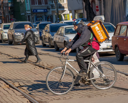 Dnepropetrovsk, Ukraine - 02.15.2022: A delivery service courier with a thermal bag on a bicycle rides around the city. home food delivery.のeditorial素材