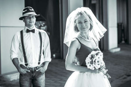 Portrait of a young couple in wedding attire celebrating their wedding anniversary in black and white. Smile, kiss, holding the bouquet together, love.の写真素材