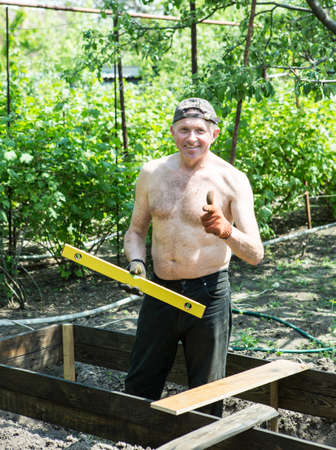 A man of mature years makes high beds on a personal plot. The master works with a level tool to...