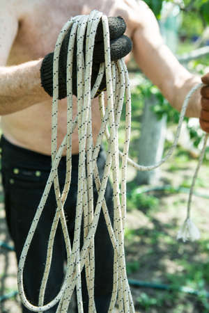 A man of mature years on a personal plot winds a rope for construction work.