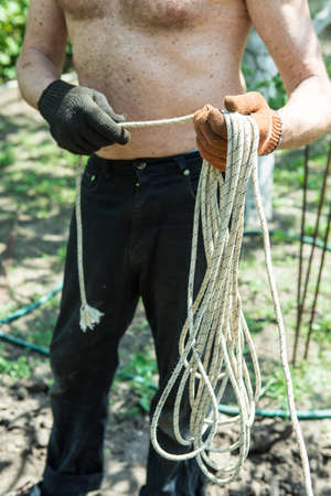 A man of mature years on a personal plot winds a rope for construction work.の写真素材