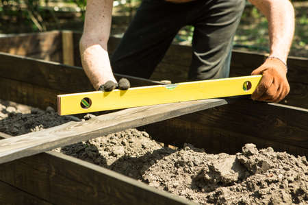 A man of mature years makes high beds on a personal plot. The master works with a level tool to...