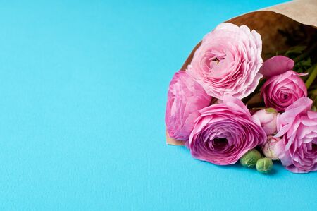 A bouquet of pink ranunculus flowers in craft wrapping paper on a blue background. Top view, copy space. Concept Mother's Day, Family Day, Valentine's Dayの写真素材