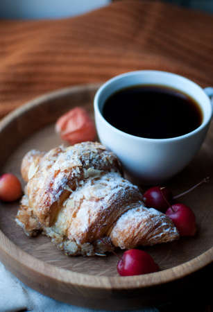 A cup of coffee and a croissant on a wooden tray with red apples
