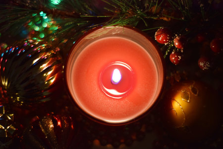 Lighted red candle in the dark with Christmas decorations.の写真素材