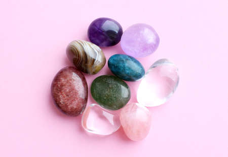 Various colored gems, uncut and tumbled. Amethyst, rose quartz, agate, apatite, aventurine on a pink...
