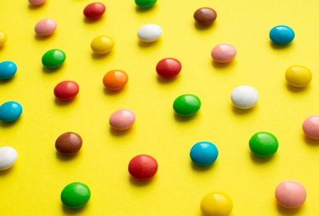 Colored balls of sugar on a yellow background. Chocolate candies covered with multicolored sugar glaze.の写真素材