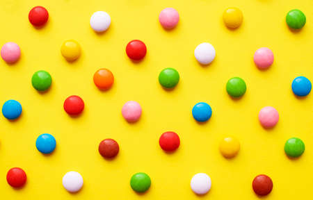 Colored balls of sugar on a yellow background. Chocolate candies covered with multicolored sugar glaze.の写真素材