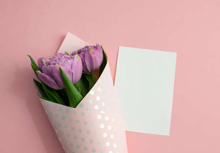 Bouquet of lilac tulips wrapped in wrapping paper. A white sheet of paper lies on pink paper. Top view, copy space. Concept for Mother's Day, Family Day, Valentine's Dayの写真素材