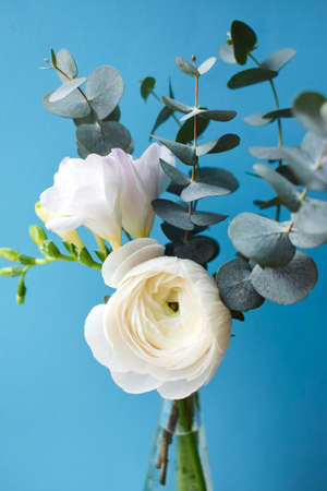 Delicate bouquet with white ranunculus and freesia flowers with eucalyptus sprigs on a blue backgroundの写真素材